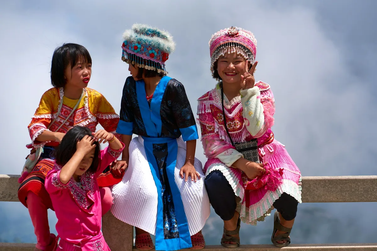 Young people in traditional Nepali dress sitting together on a hillside railing